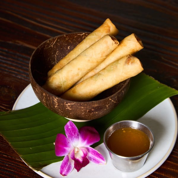 Crispy Thai spring rolls in a coconut shell, with a purple orchid and dipping sauce.
