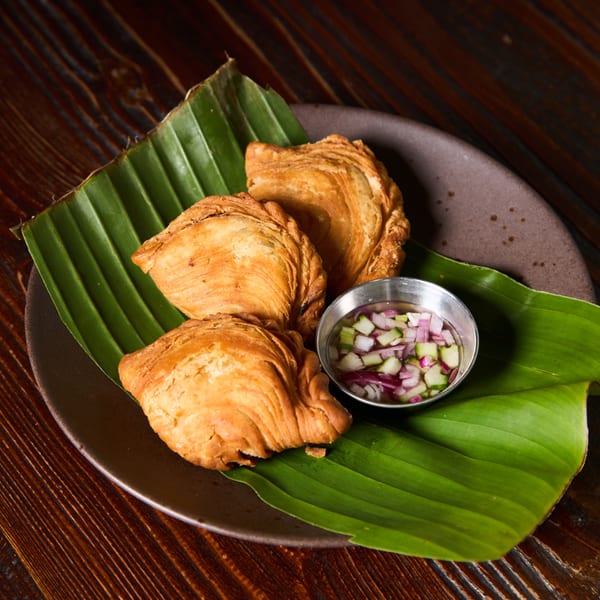 Three golden-brown Thai curry puffs on banana leaves with a side of dipping sauce.