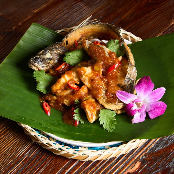 Crispy fried fish with chili sauce, cilantro, and a purple orchid on a banana leaf.