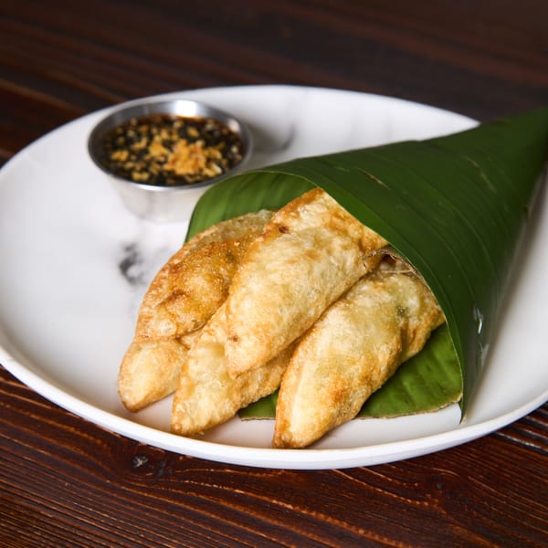 Golden fried Thai dumplings, wrapped in a banana leaf, served with a dark dipping sauce.