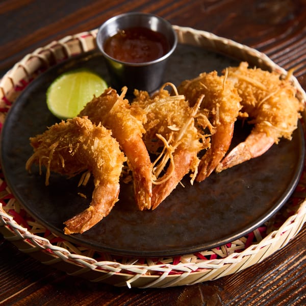 Crispy fried shrimp with shredded coconut, a lime wedge, and dipping sauce on a dark plate.