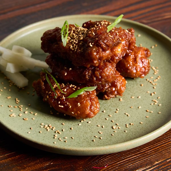 Sweet and spicy Thai chicken wings, garnished with sesame seeds and green onions, on a green plate.