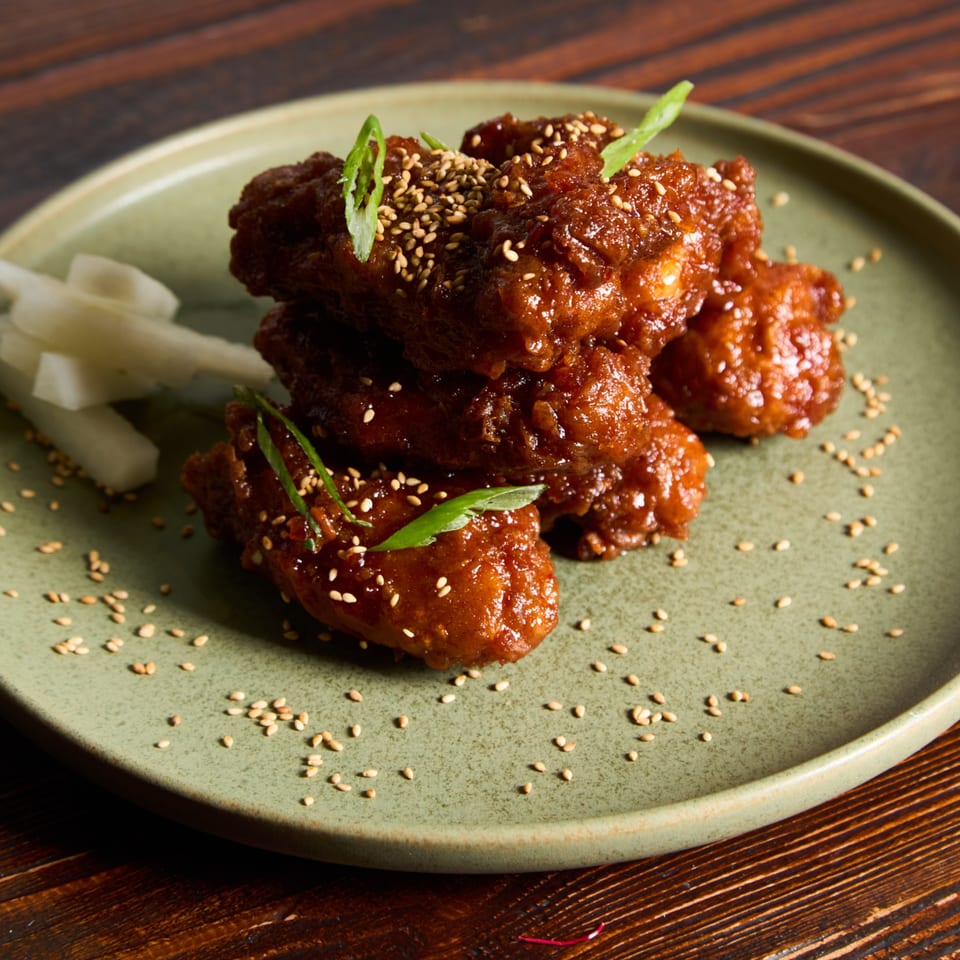 Sweet and spicy Thai chicken wings, garnished with sesame seeds and green onions, on a green plate.
