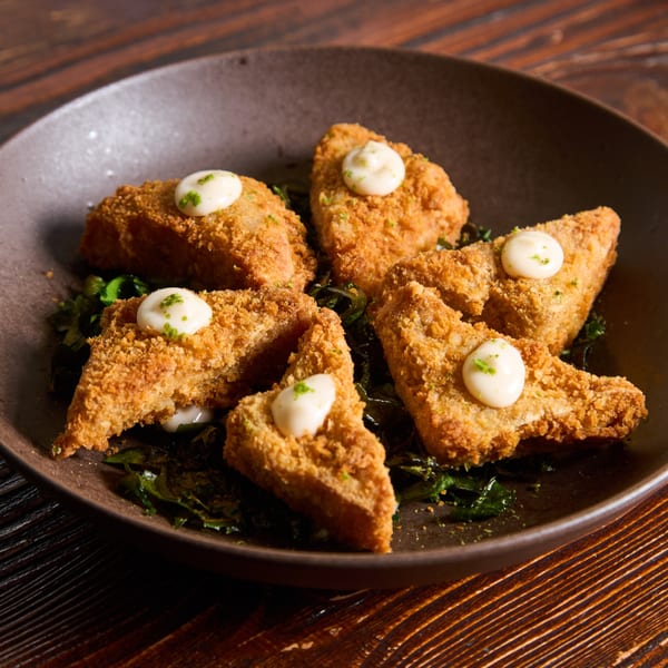 Crispy golden-brown fried tofu triangles with creamy white sauce and green garnish, served on dark greens.